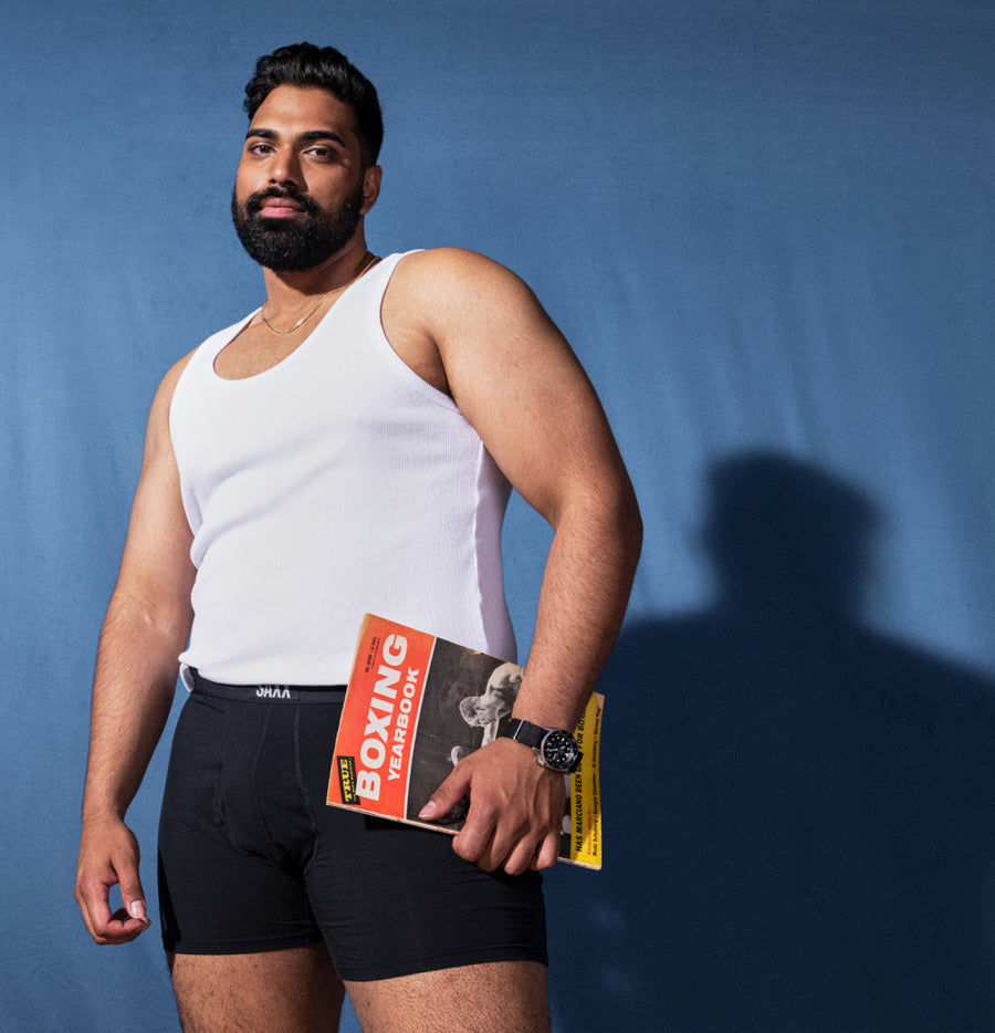 Man holding a magazine while wearing black boxer briefs and white tank top